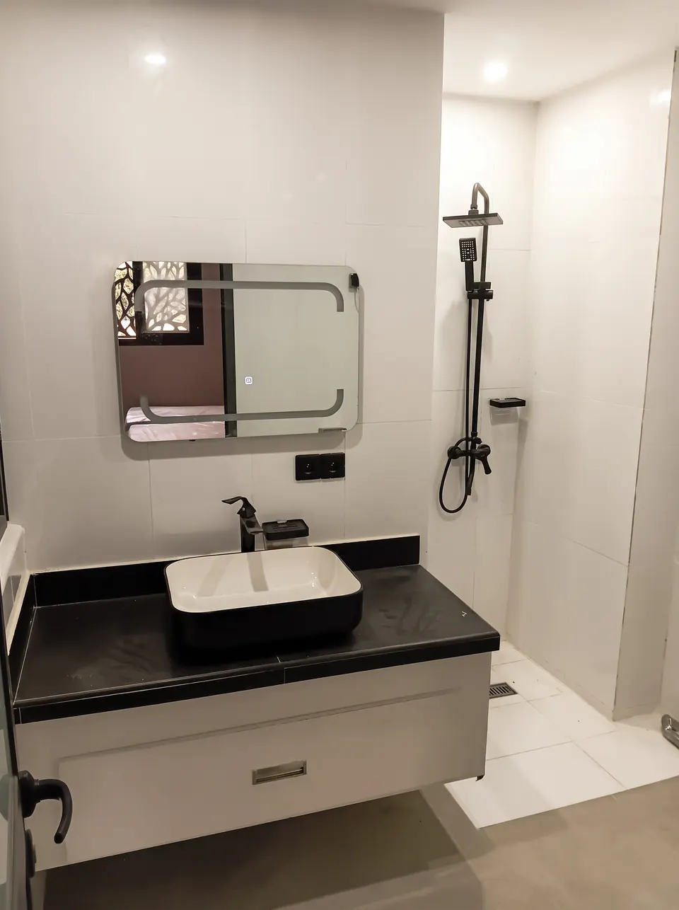 Salle d'eau avec vasque posée sur un meuble noir, miroir lumineux et douche